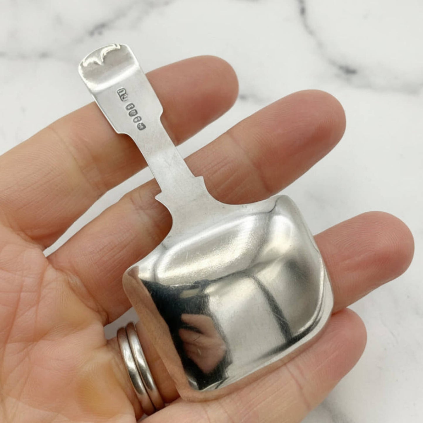 Silver spoon back held in a hand against a marble background
