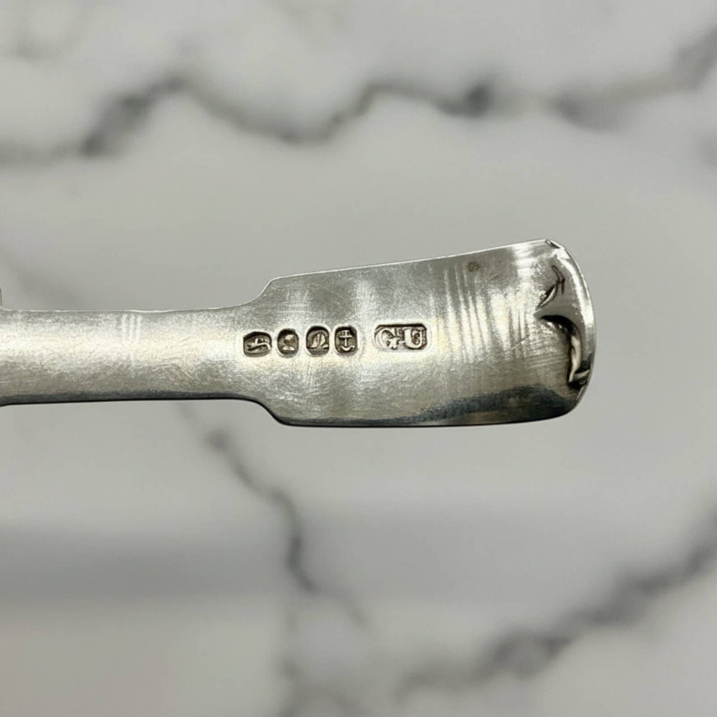 Close-up of a silver spoon handle with hallmarks details on a marble background
