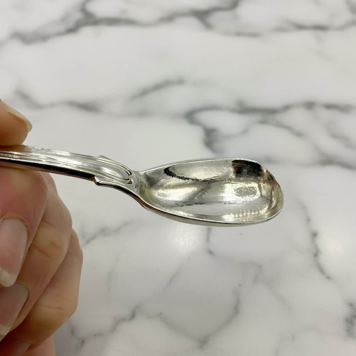 Silver spoon held by a hand against a marble background