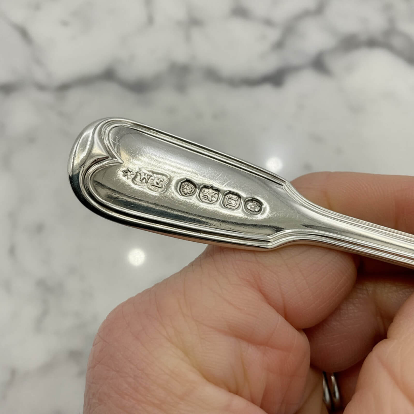 Silver spoon held by a hand with a marble background