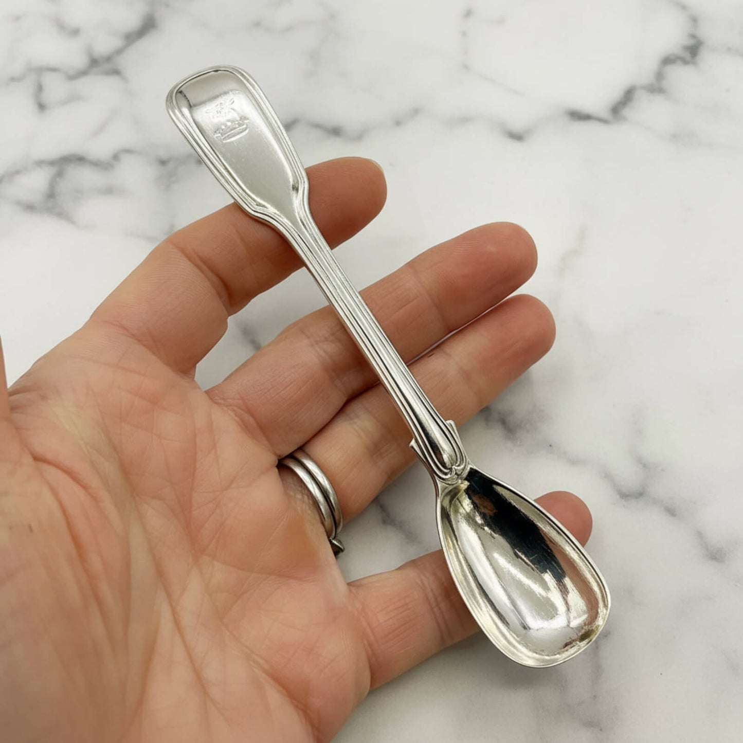 Silver spoon held in a hand against a marble background