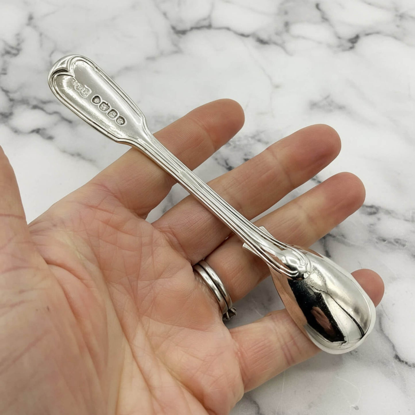 Silver spoon held in a hand against a marble background