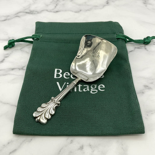 Silver caddy spoon on a green drawstring bag with 'Beeches Vintage' text on a marble background