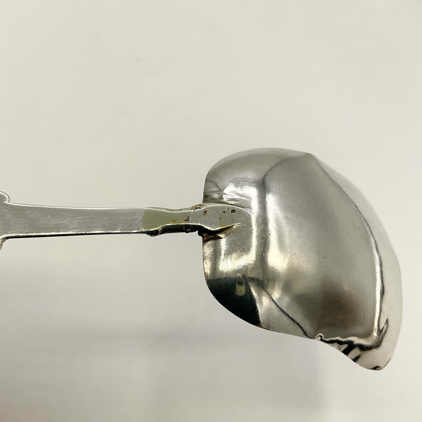 Back of silver caddy spoon handle showing a repair on a white background