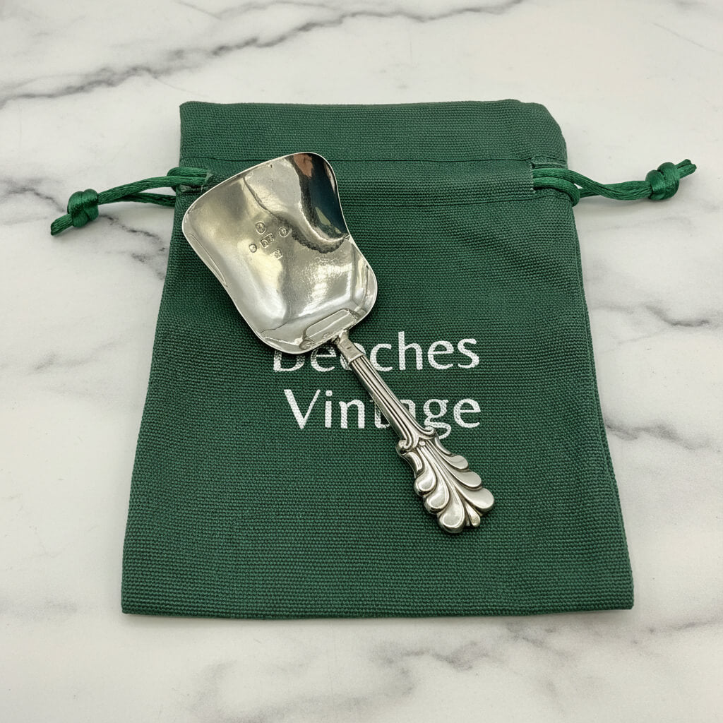 Silver caddy spoon on a green drawstring bag with 'Beeches Vintage' text on a marble background