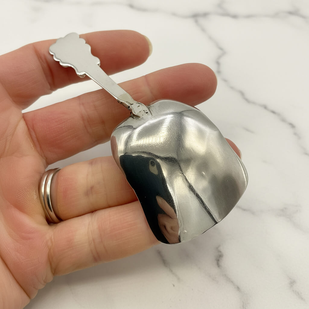 silver caddy spoon held upside down in a hand with a marble background