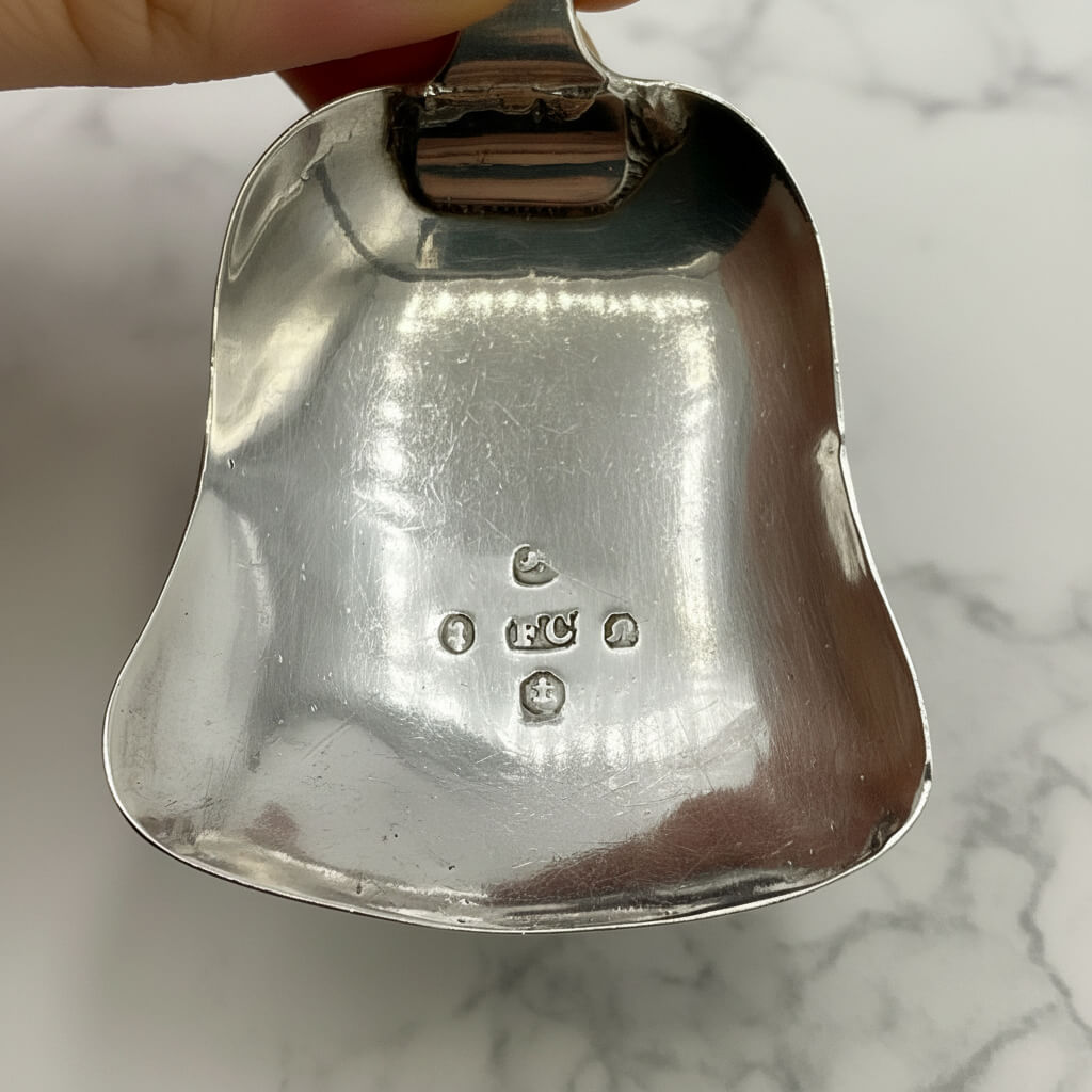 Close-up of a silver scoop spoon with visible hallmarks on a marble surface