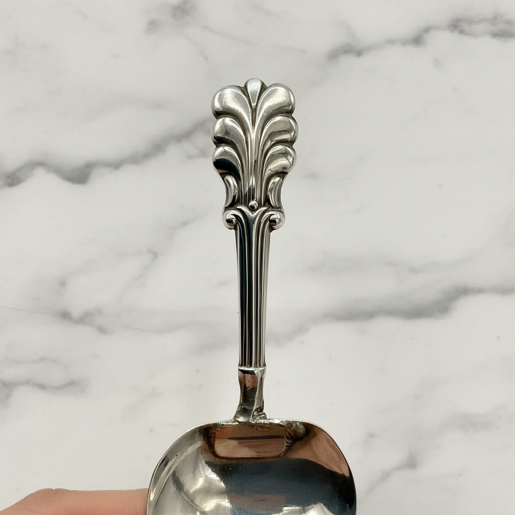 Decorative silver caddy spoon handle held against a marble background