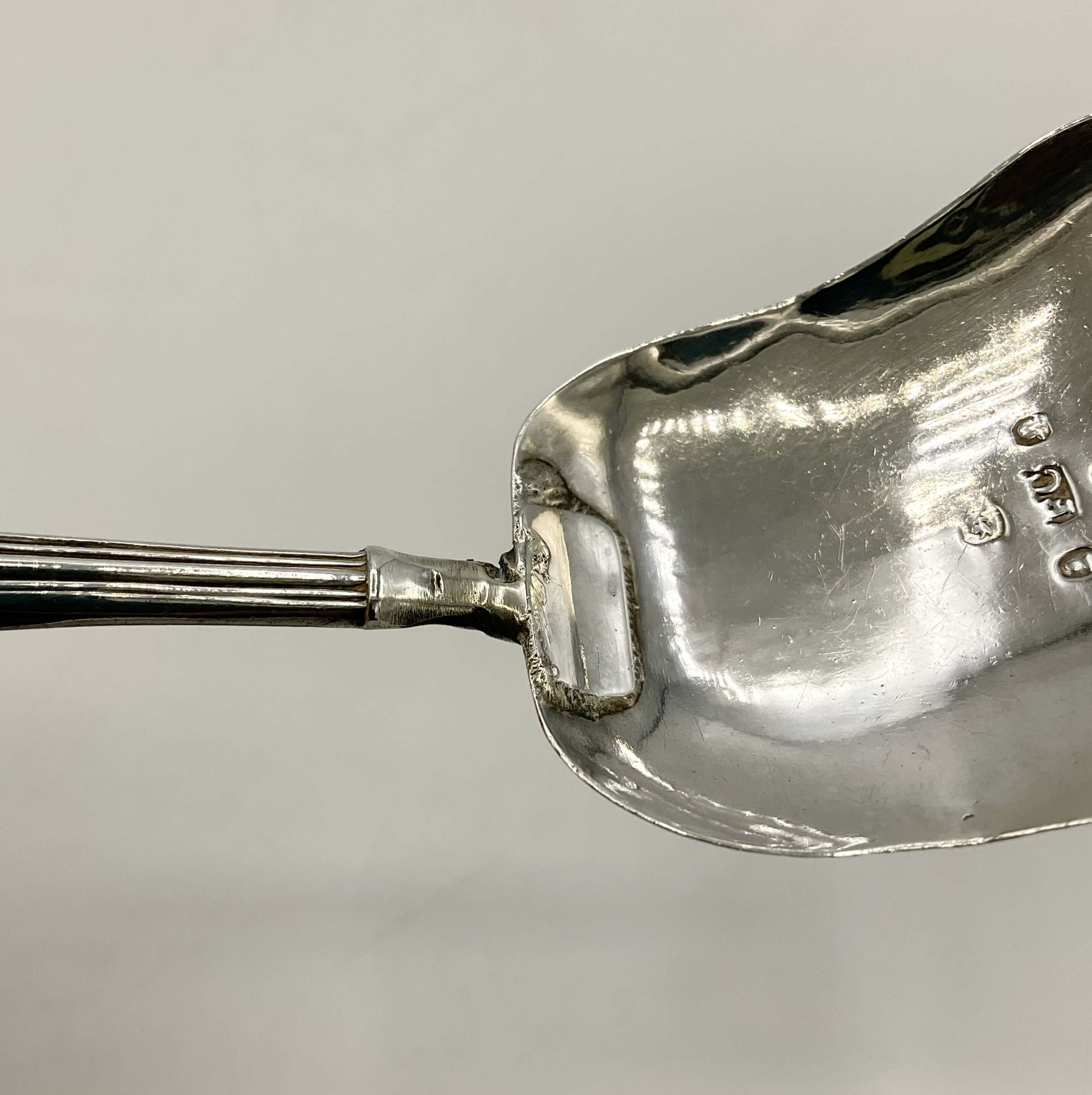 close up of silver caddy spoon handle with a repair on a white background