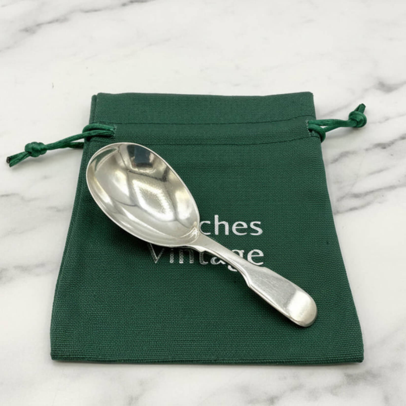 Silver spoon on a green drawstring bag with 'Beeches Vintage' text on a marble surface