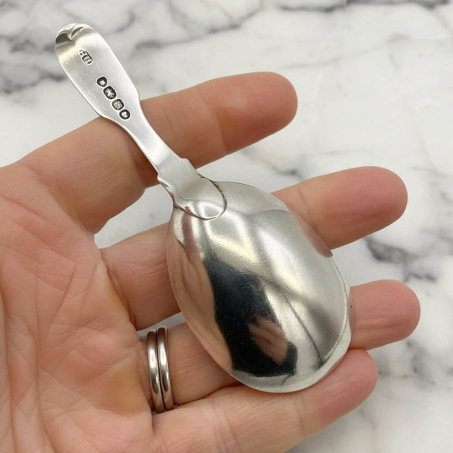 Silver spoon held in a hand with a marble background