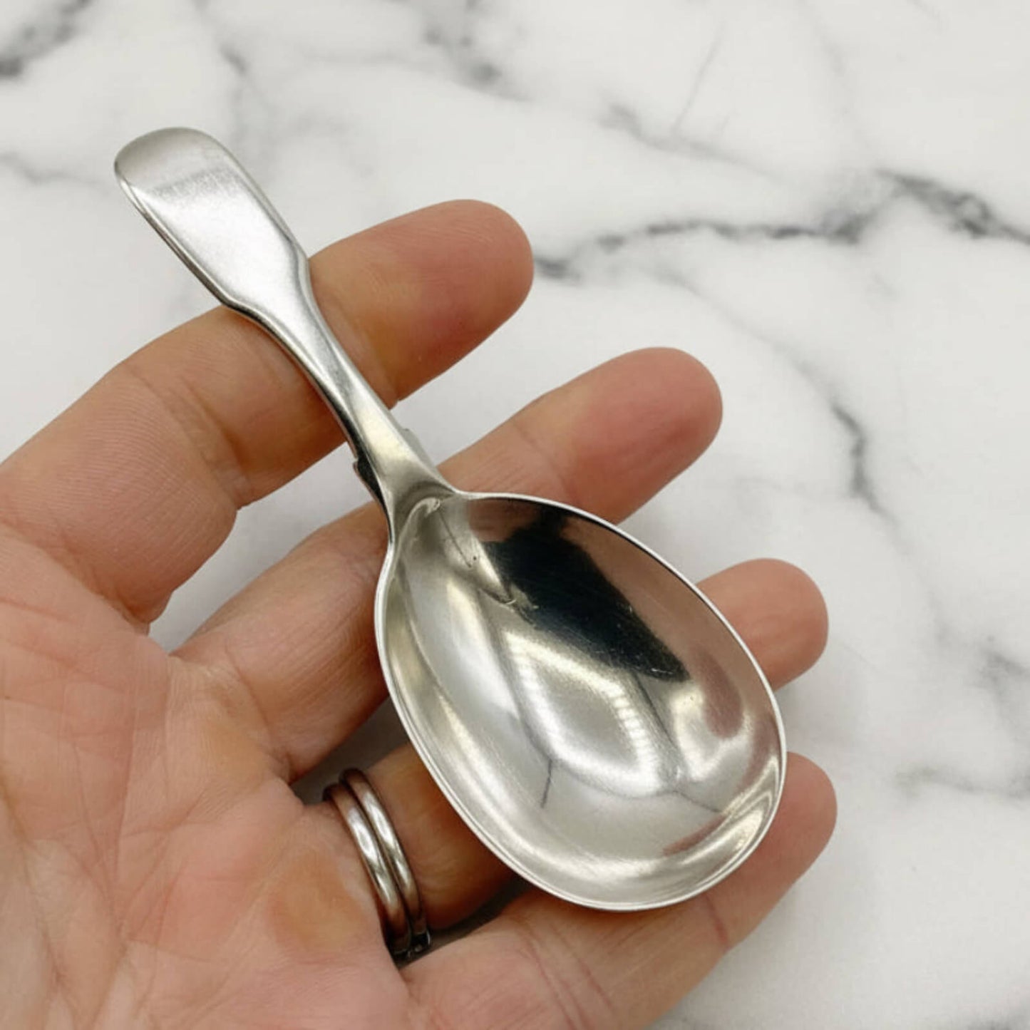 Silver spoon held in a hand against a marble background