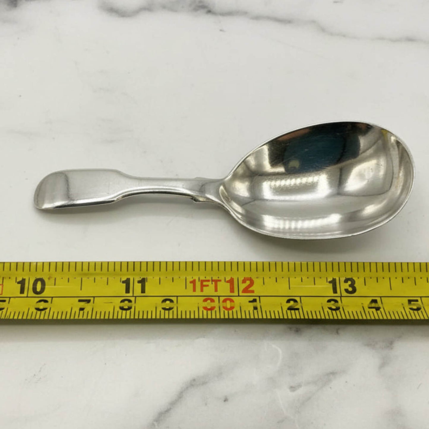 Silver spoon on a marble surface with a measuring tape for scale.