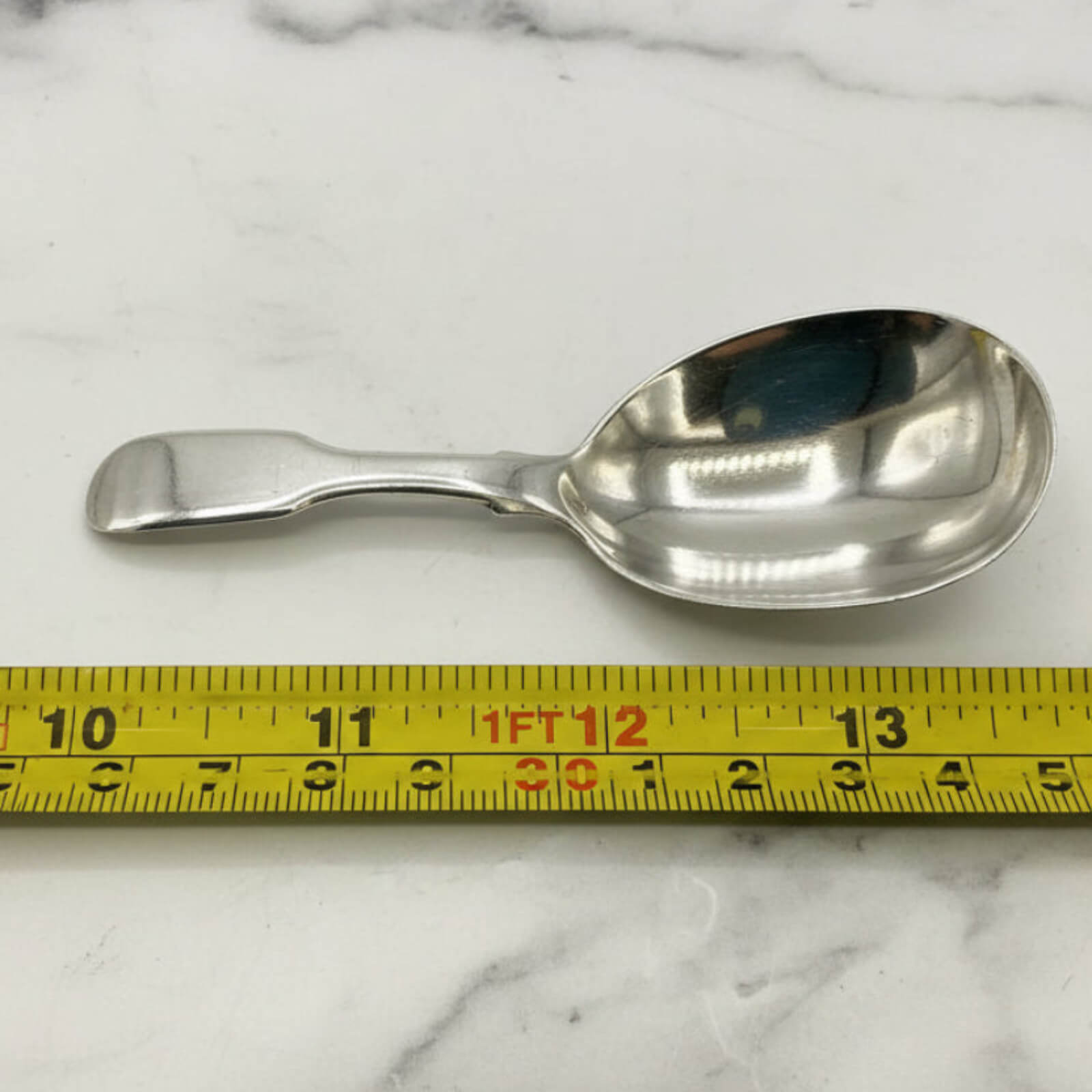 Silver spoon on a marble surface with a measuring tape for scale.