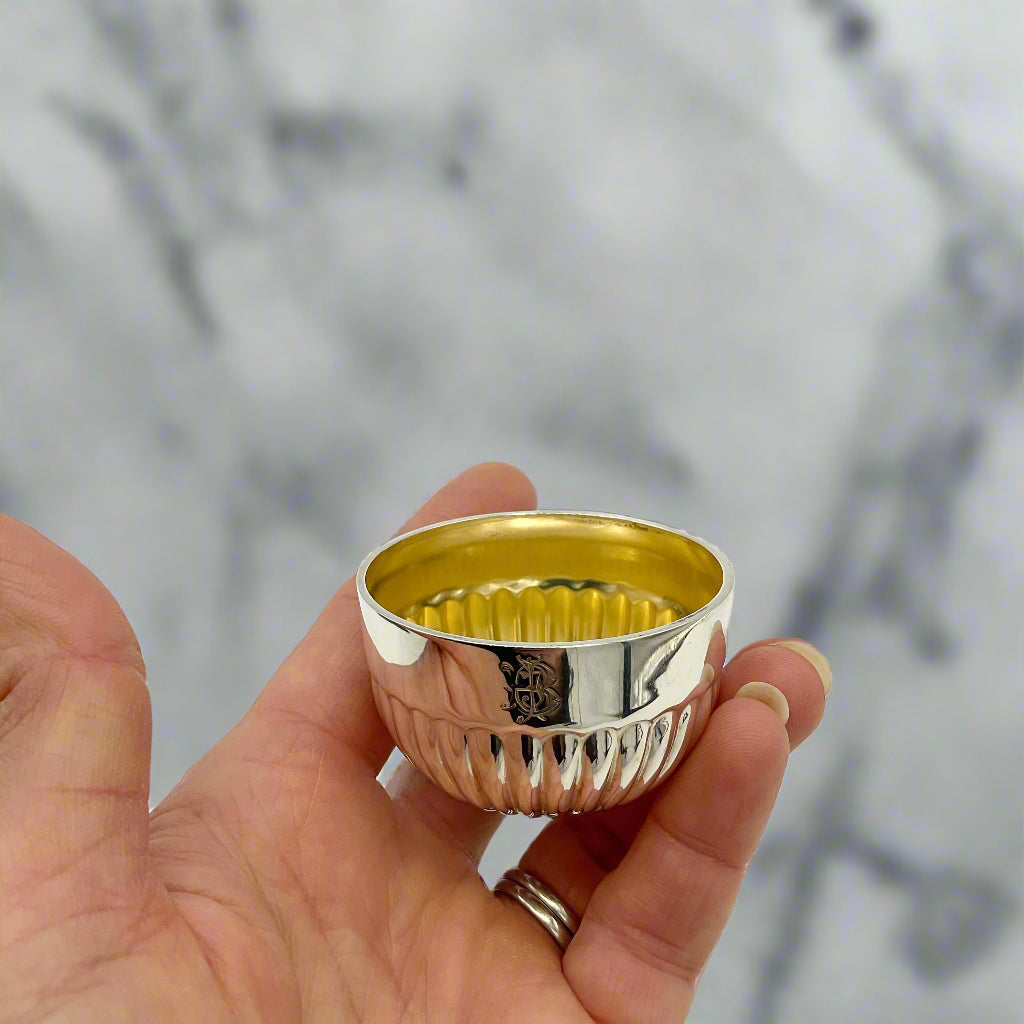 Glided silver Victorian salt held in a hand with a marble background 