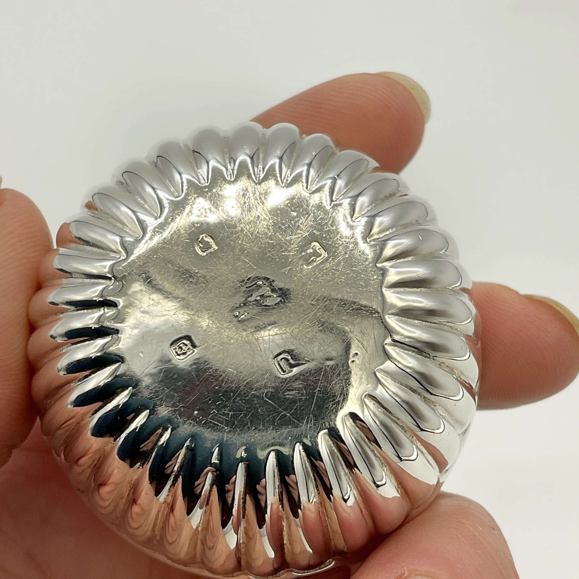 Base of Glided silver Victorian salt held in a hand showing the hallmarks with a white background 