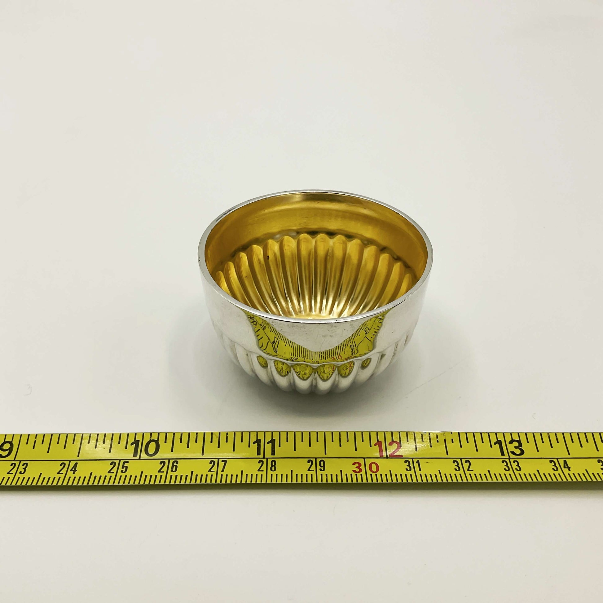 Glided silver Victorian salt next to a tape measure showing the  diameter as 2.5cm on a white background 