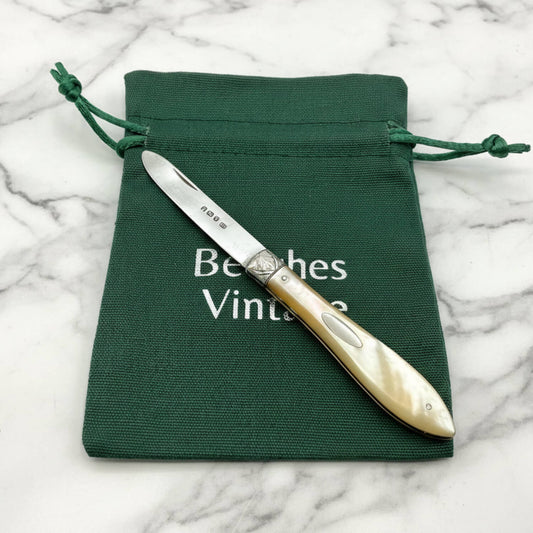 Knife with decorative handle on a green drawstring bag with 'Beeches Vintage' text, on a marble surface.