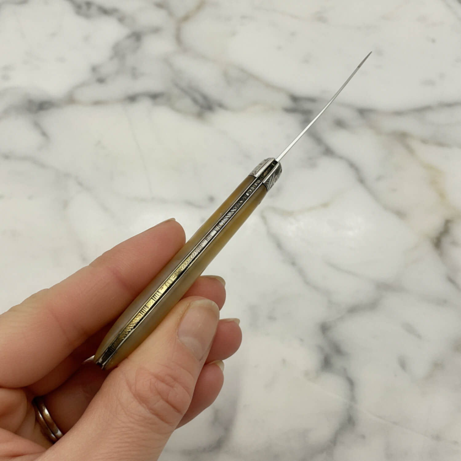 Hand holding a fruit knife showingthe back on a marble background