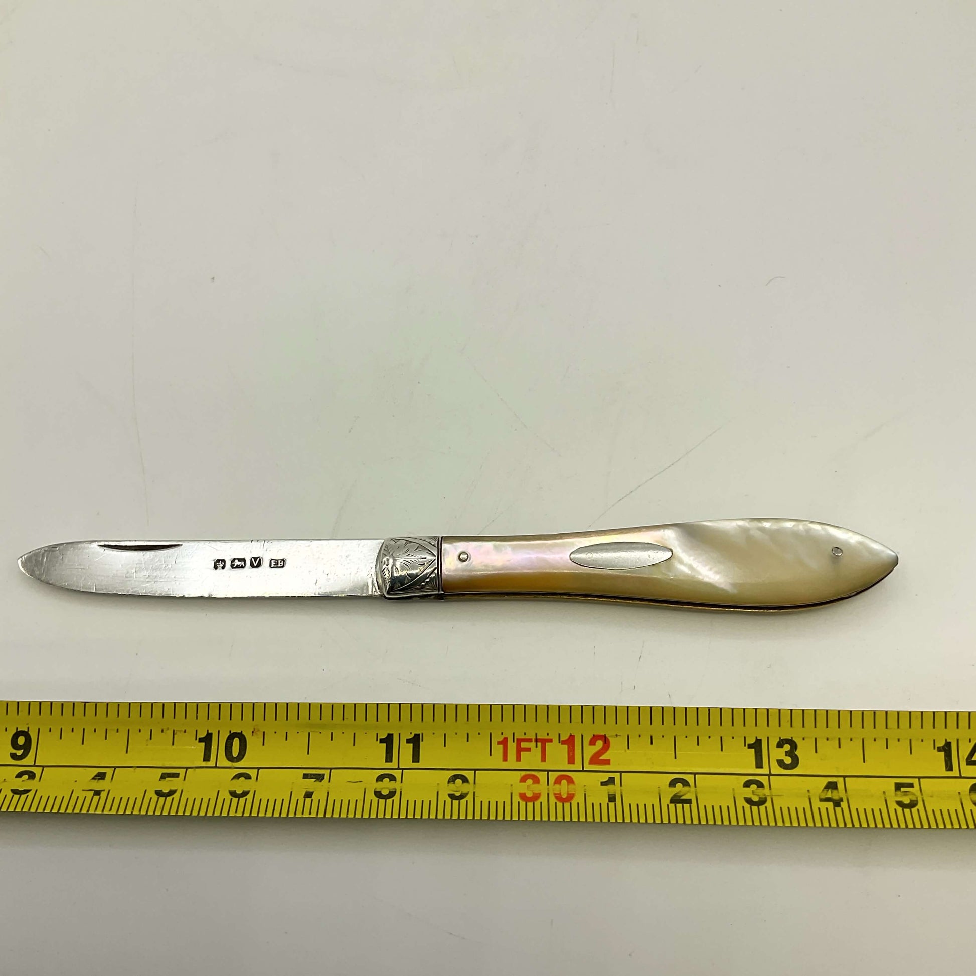 Silver knife with decorative handle on a white background, measured by a yellow ruler.