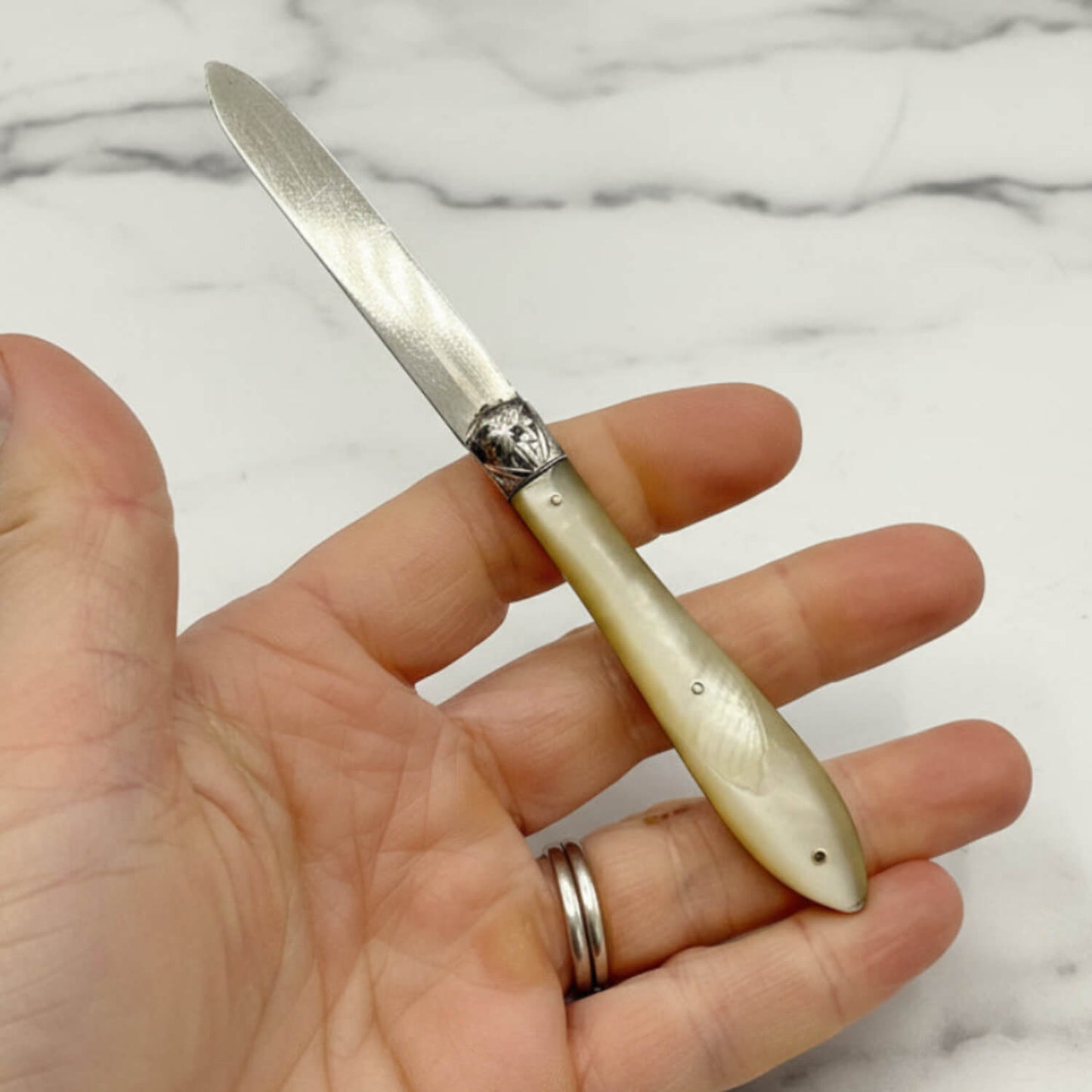 Hand holding a decorative knife with a pearl handle on a marble background