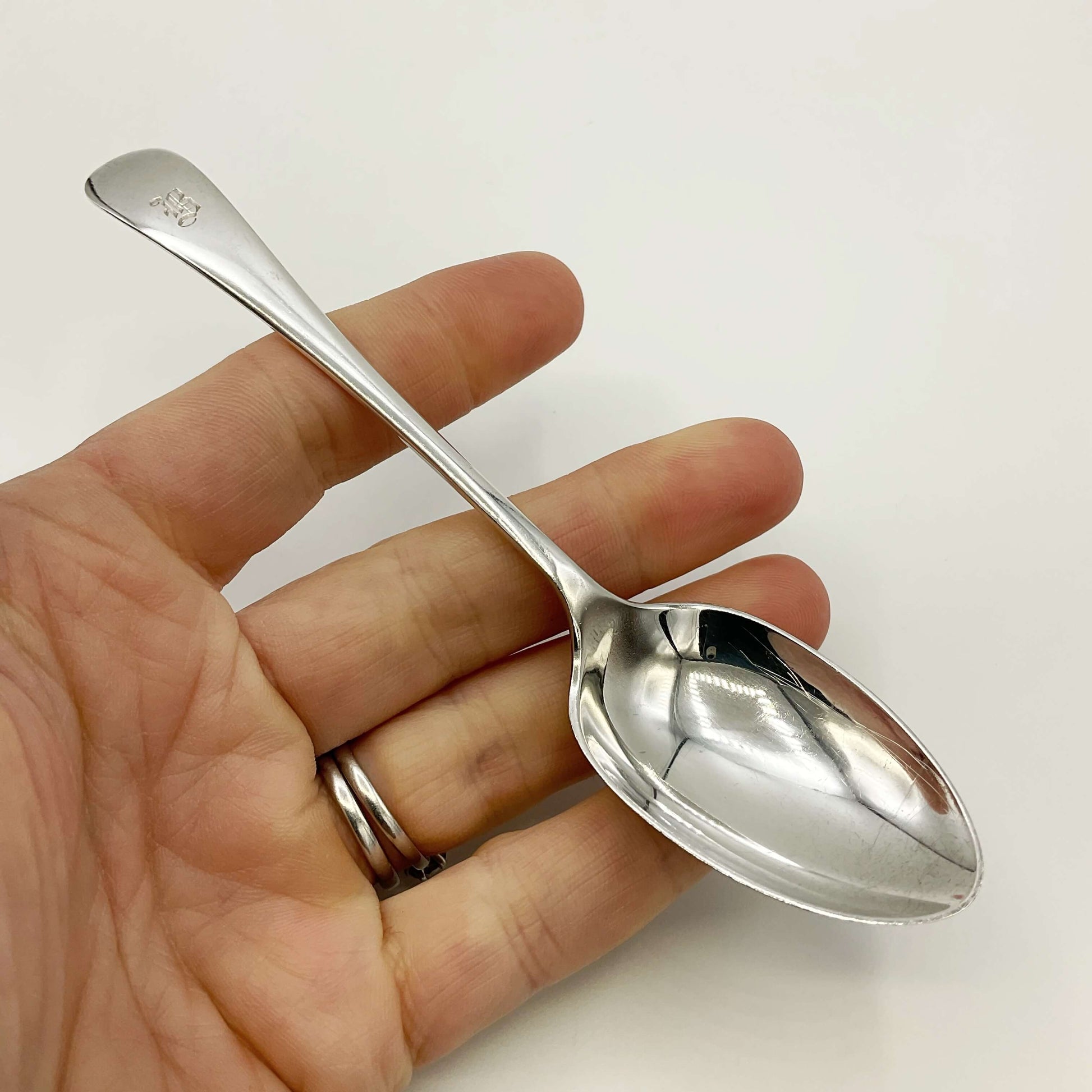 Antique silver teaspoon held in a hand on a white background 