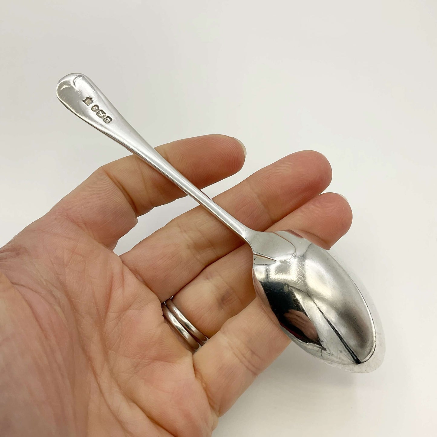 The back of an Antique silver teaspoon held in a hand on a white background 