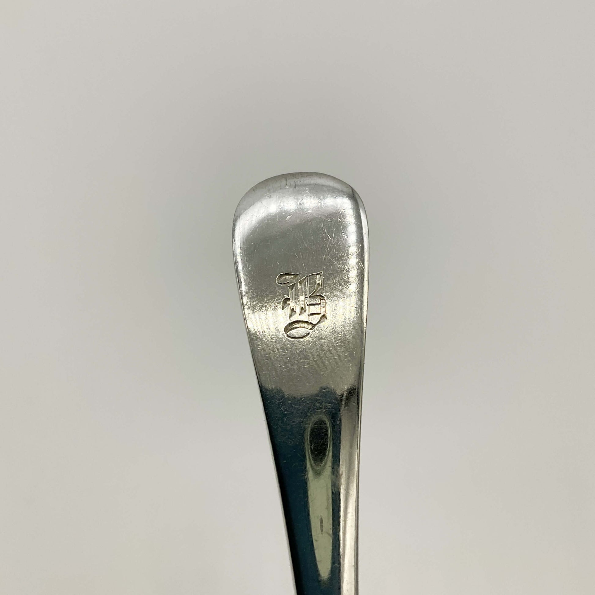 The handle of an antique silver easp showing a gothic letter B engraved on the handle with a white background 