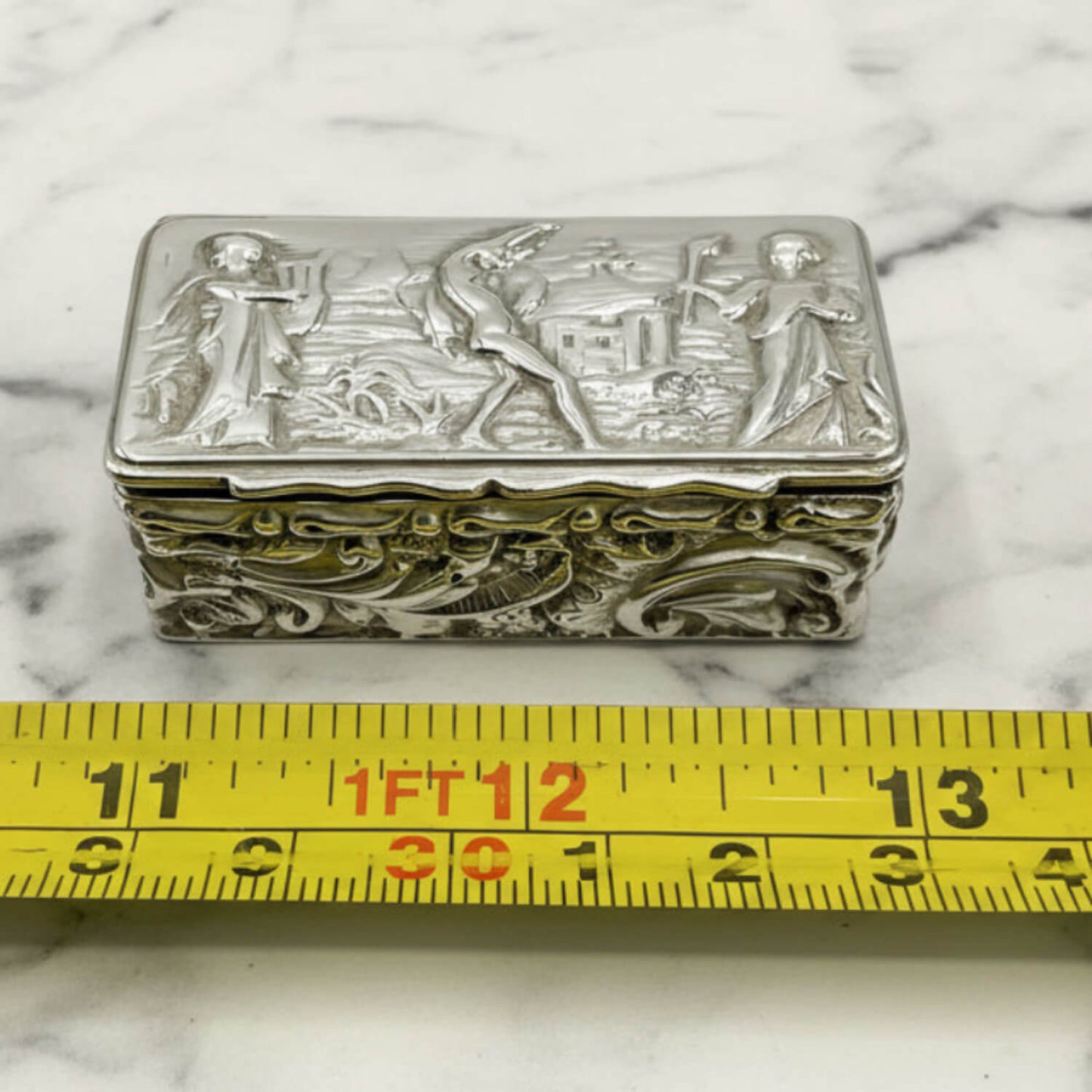 Decorative silver box on a marble surface with a measuring tape for scale.
