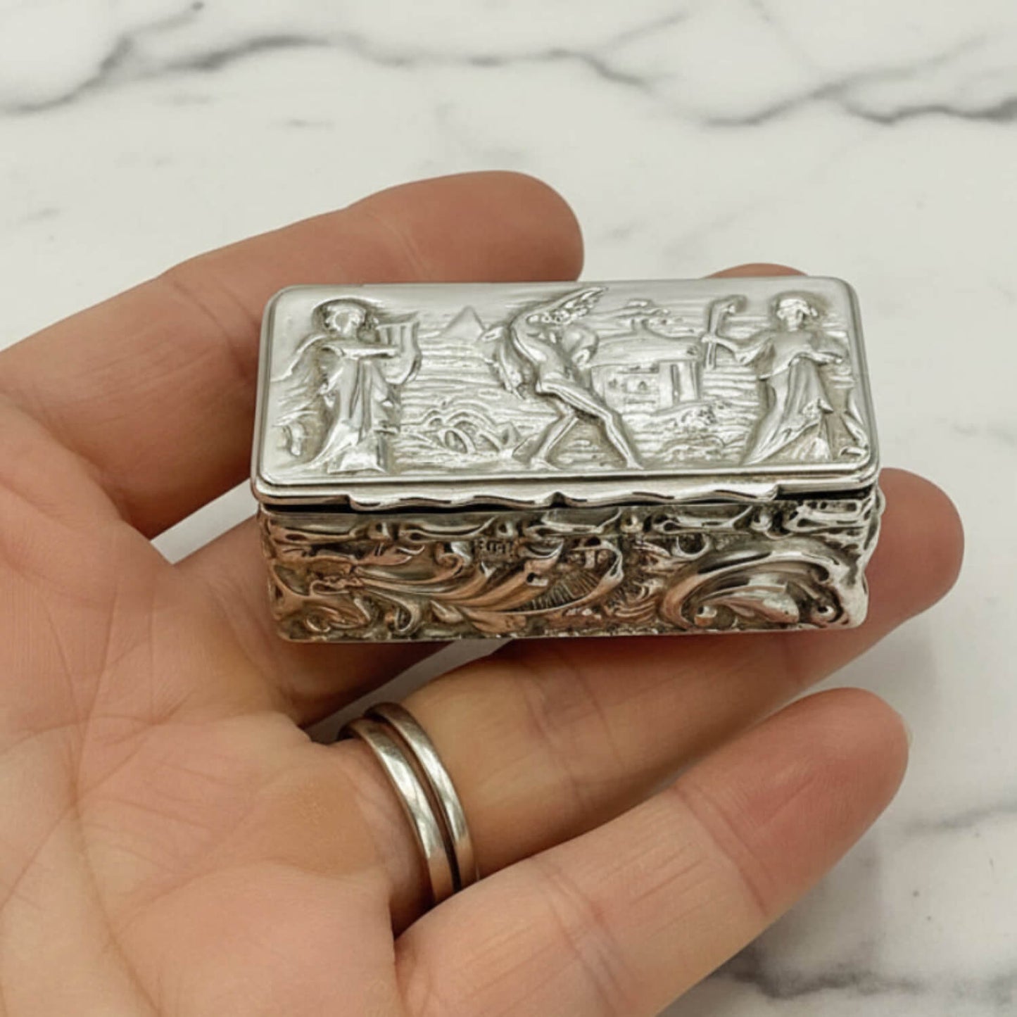 Decorative silver box held in a hand with a marble background