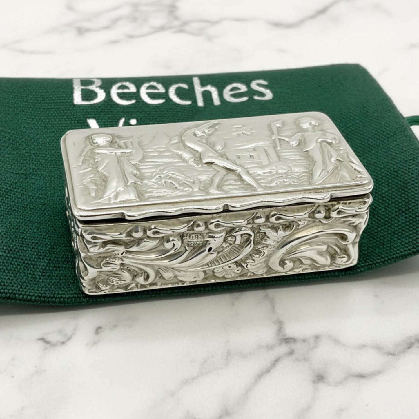 Decorative silver box with intricate designs on a green bag background