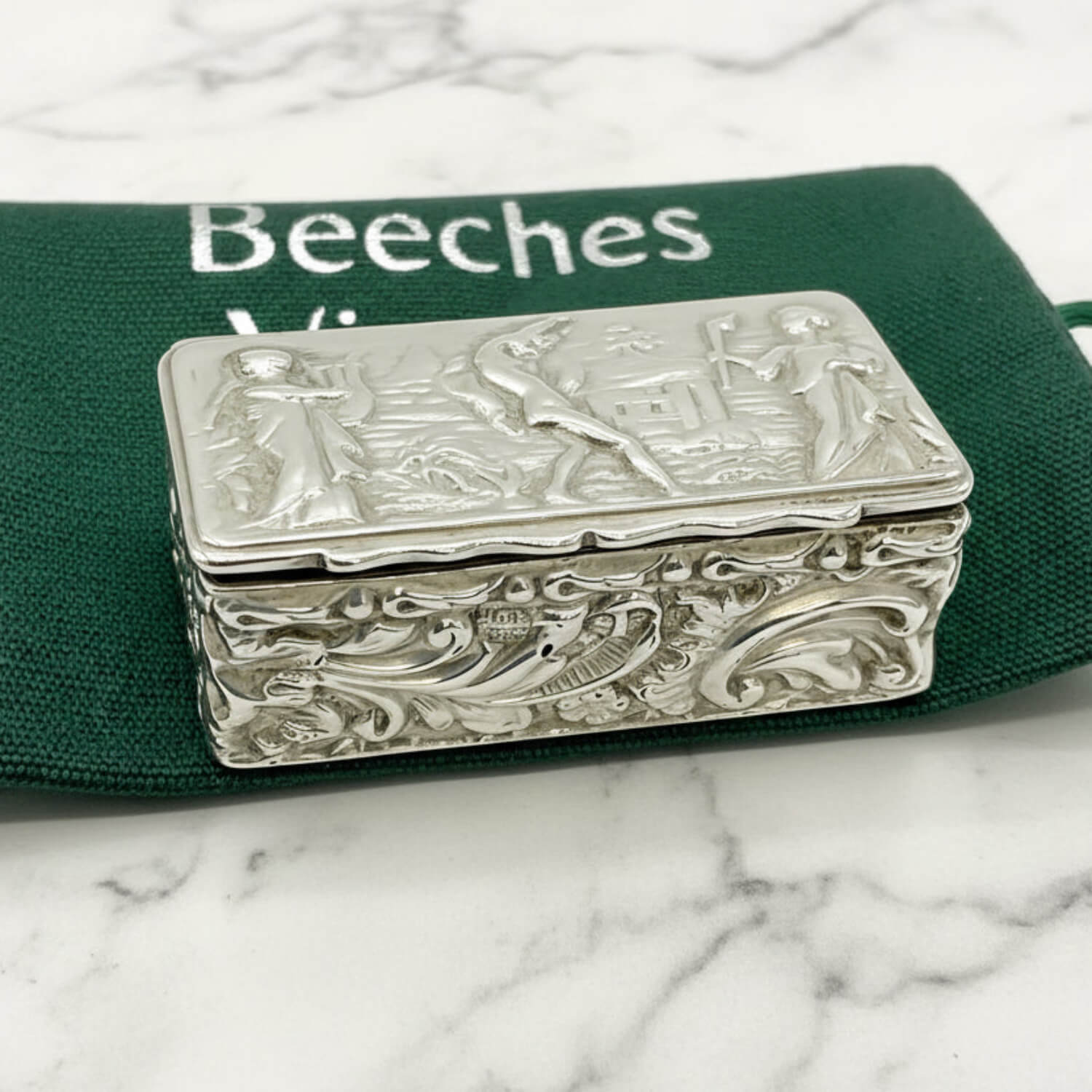 Decorative silver box with intricate designs on a green bag background