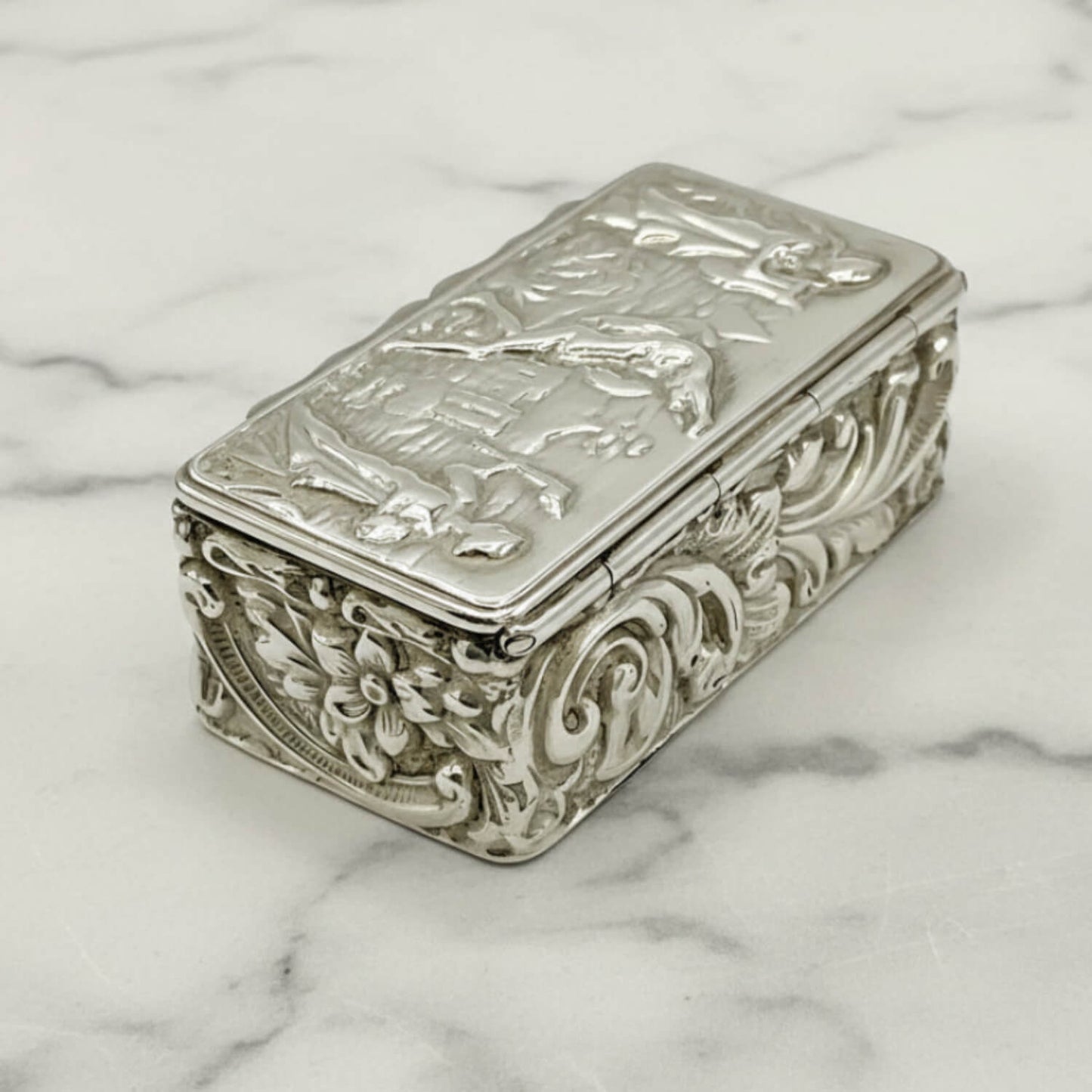 Decorative silver box with intricate designs on a marble surface
