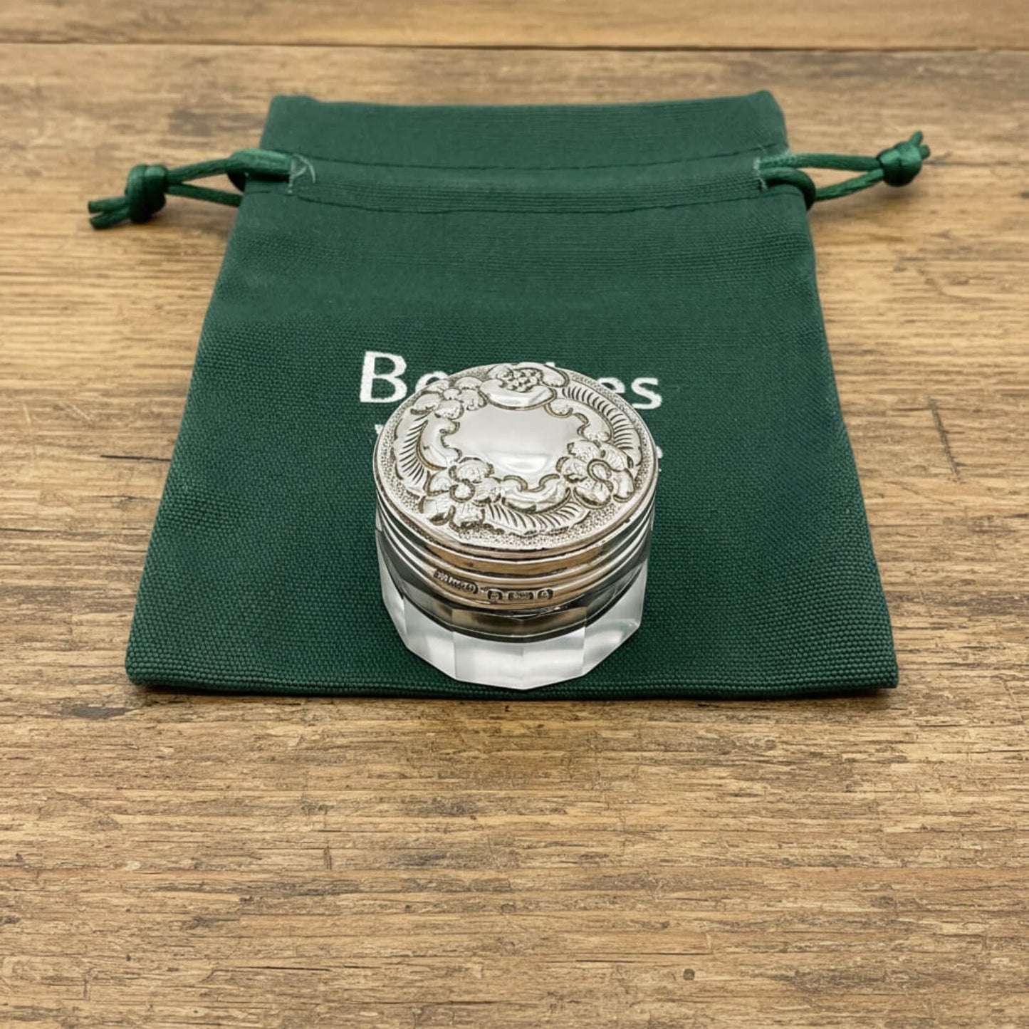 Silver decorative item on a clear stand with a green drawstring bag labeled 'Bentley' in the background.
