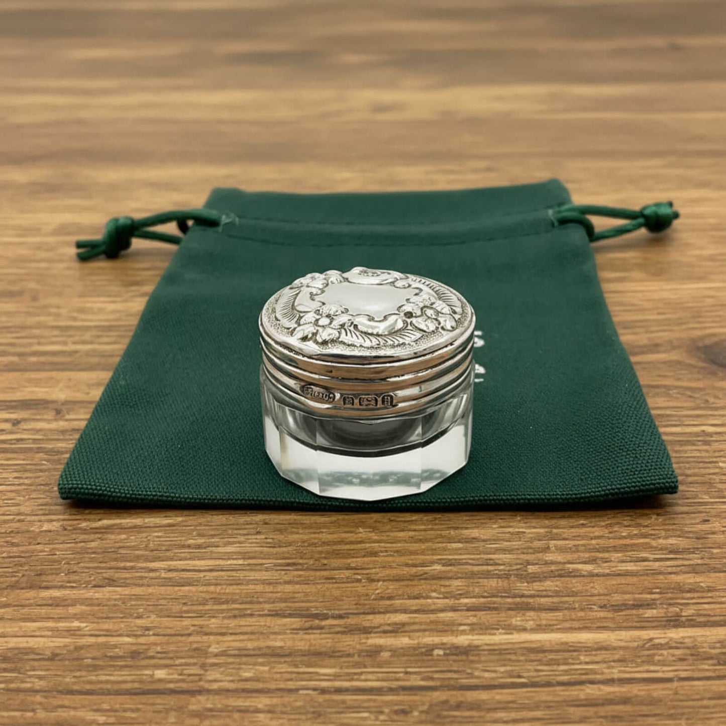 Silver decorative jar on a green cloth with a wooden background