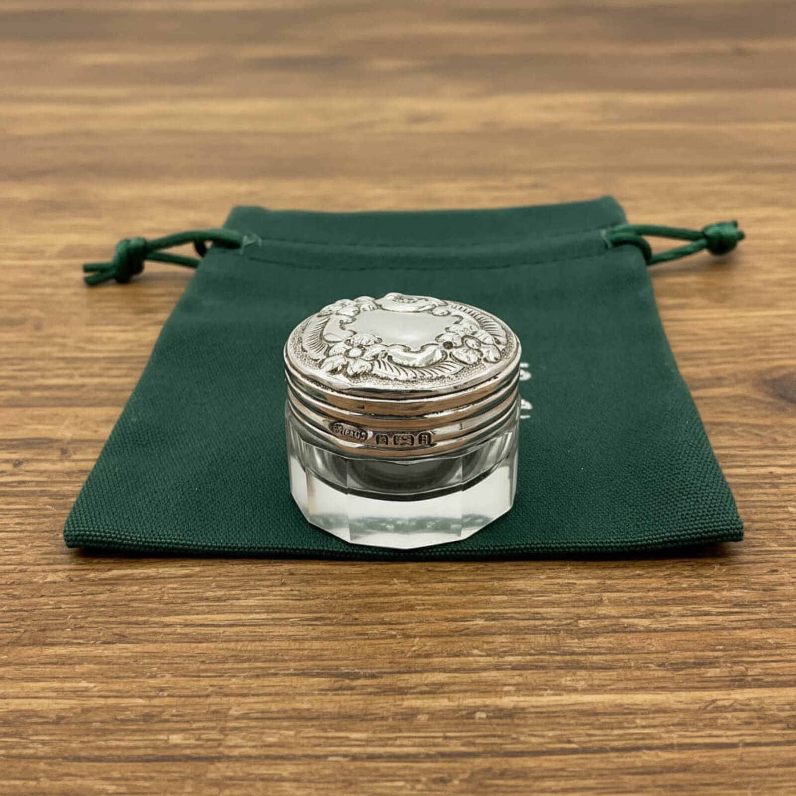 Silver decorative jar on a green cloth with a wooden background