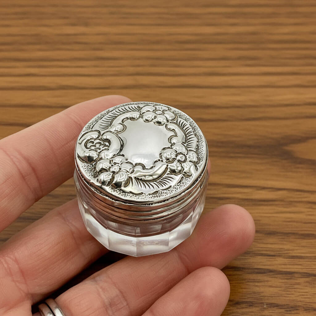 Silver decorative container held in a hand on a wooden surface