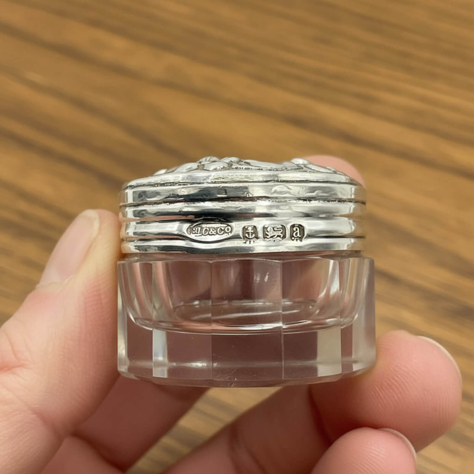 Clear glass jar with silver lid held in a hand against a wooden background