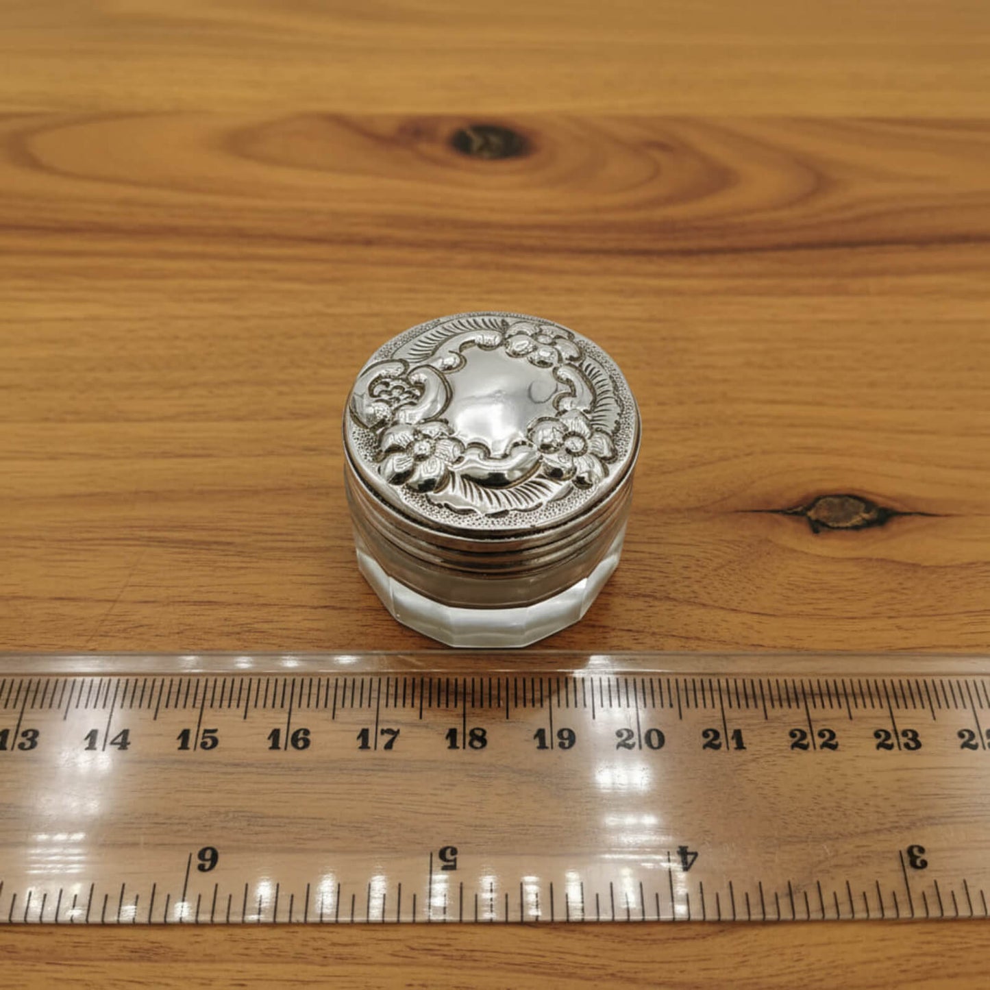 Decorative silver container on a wooden surface with a ruler for scale.