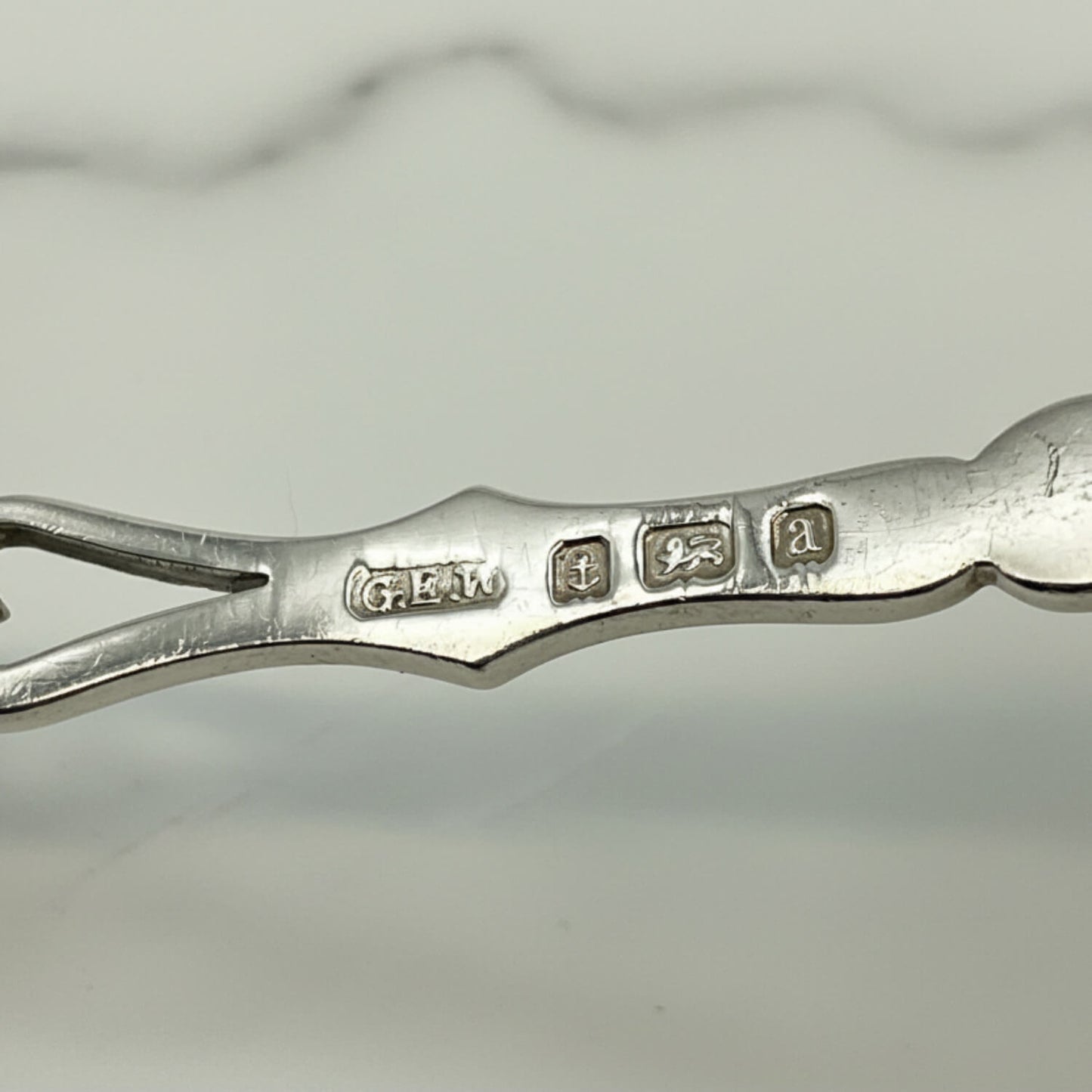 Close-up of a spoon handle showing engraved hallmarks, photographed on a light gray background.