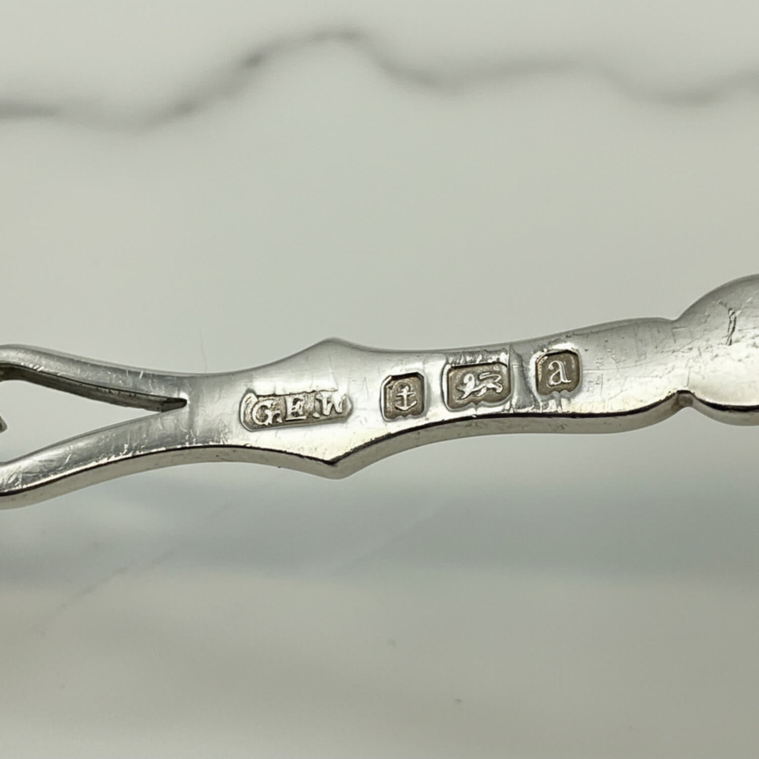Close-up of a spoon handle showing engraved hallmarks, photographed on a light gray background.
