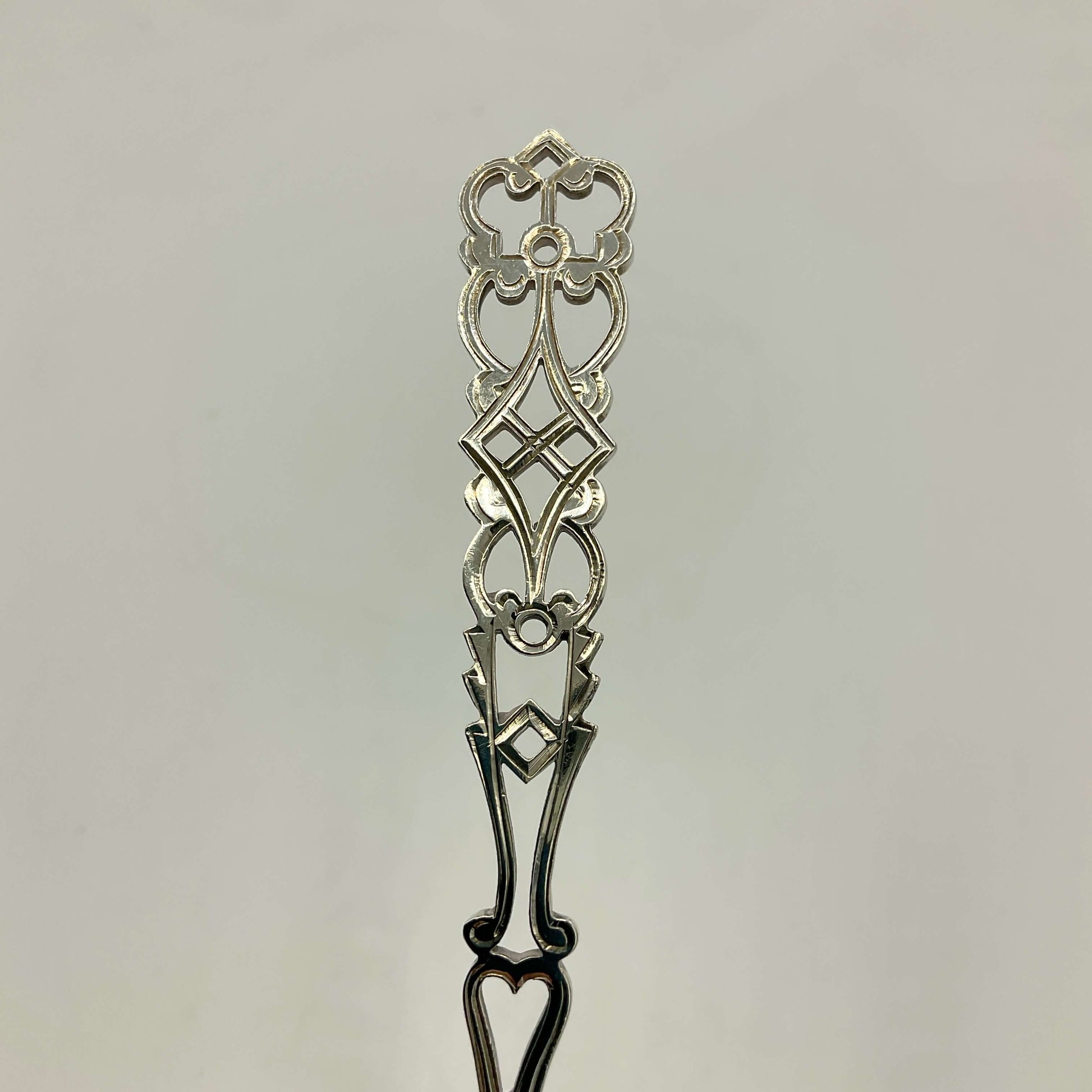 An ornate silver sifter spoon handle shown against a plain light gray background.