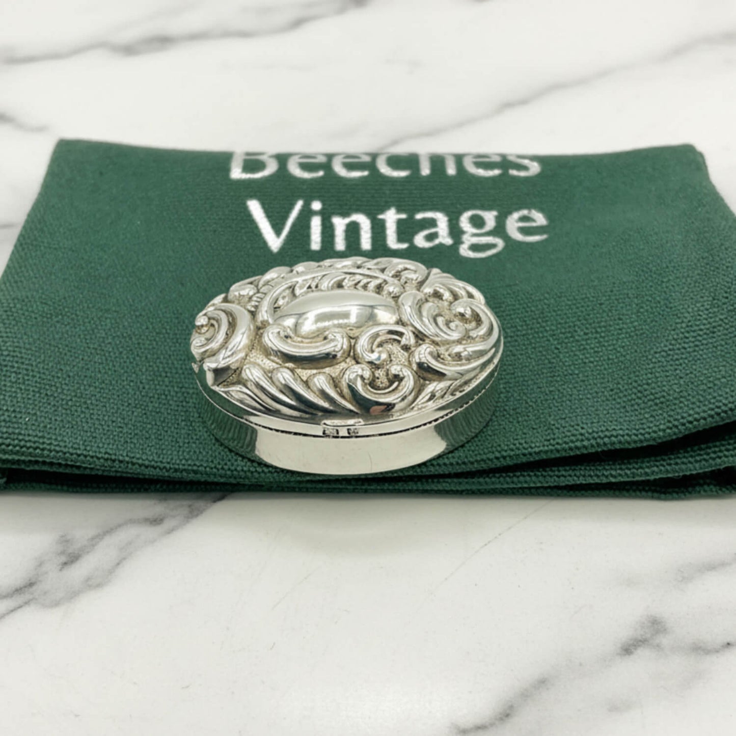 Decorative silver pill box on a green cloth bag with 'Beeches Vintage' branding.