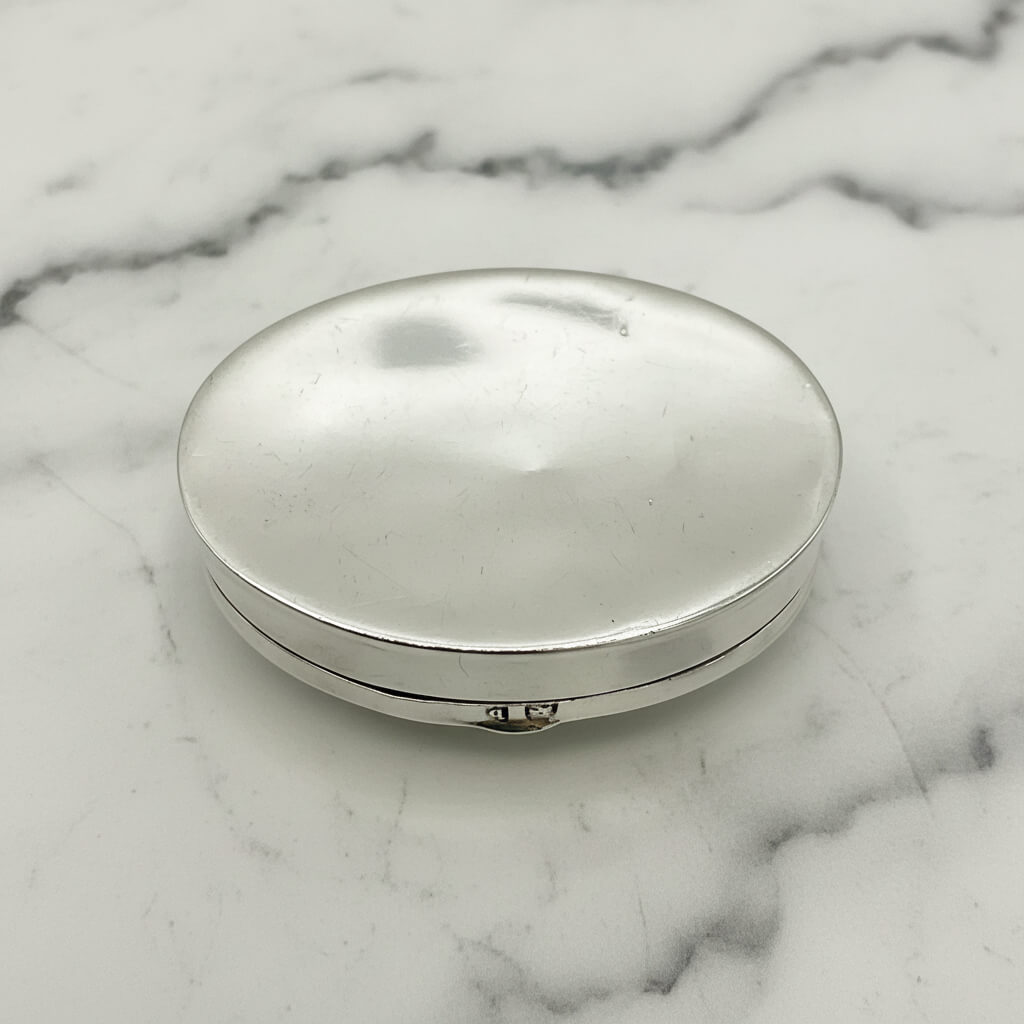 base of a silver pill box on a marble surface