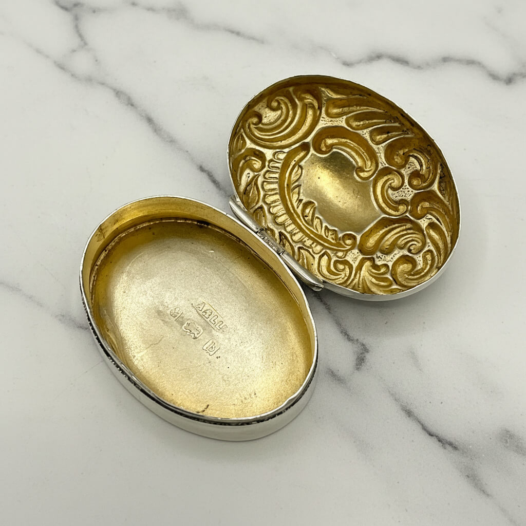 Decorative gold and silver pill box with the lid open on a marble surface