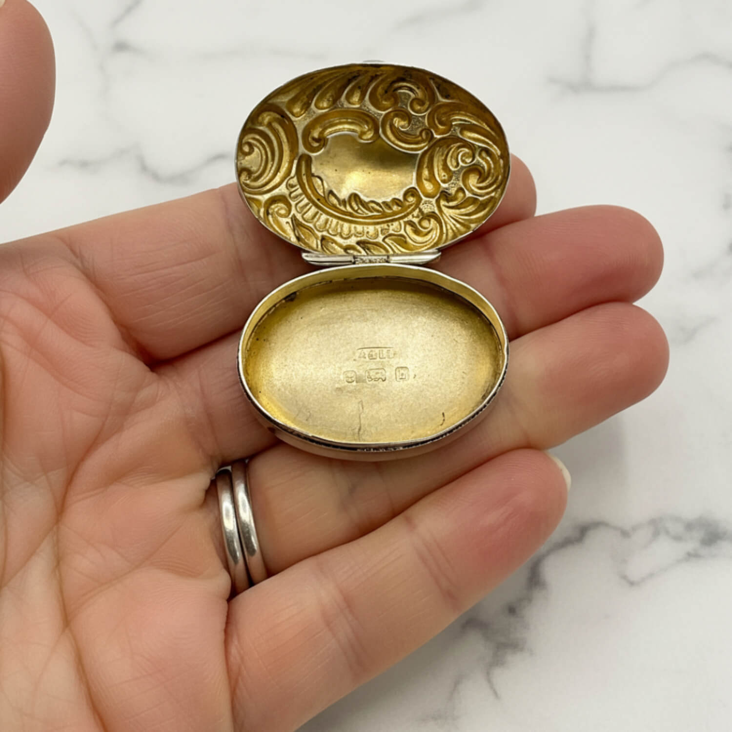 Antique 1901 Sterling Silver Pill Box open with gold interior held in a hand with a marble surface