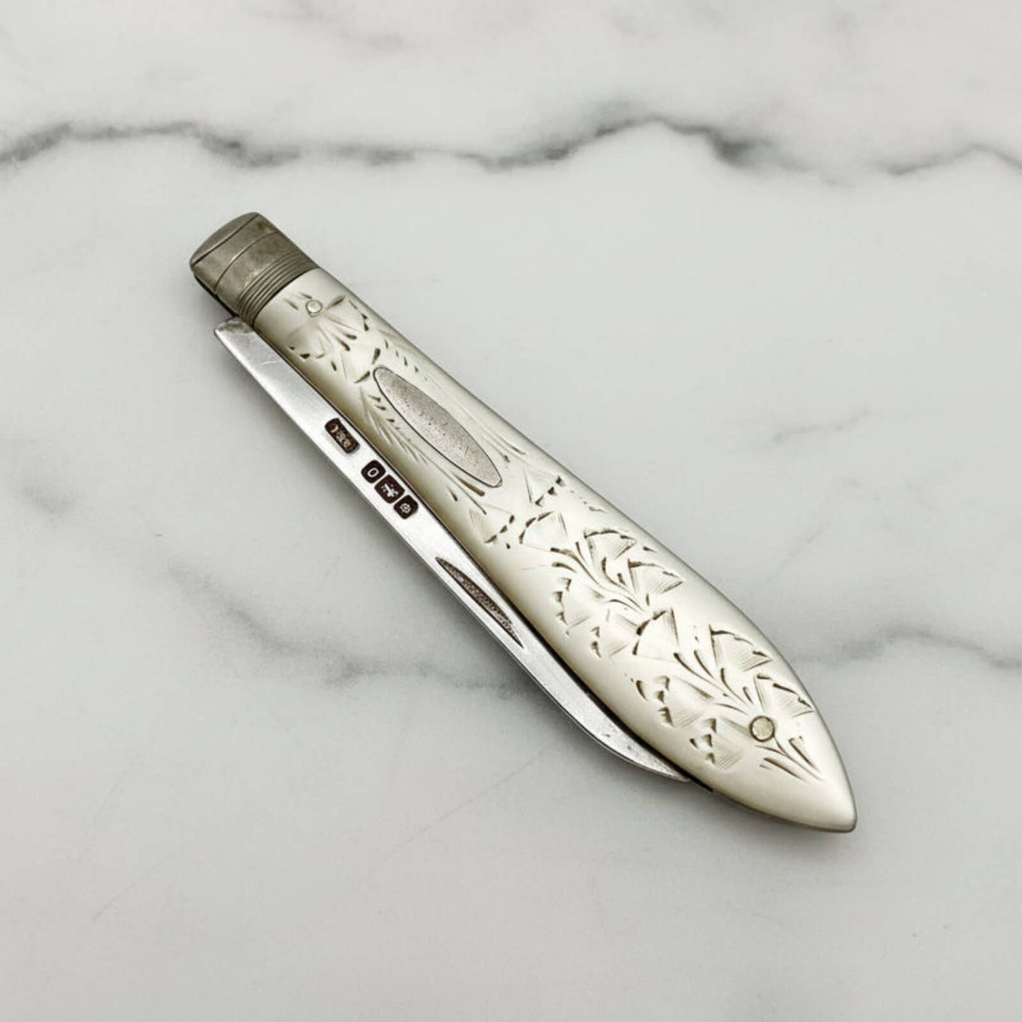 Decorative silver fruit knife with intricate patterns on a marble background