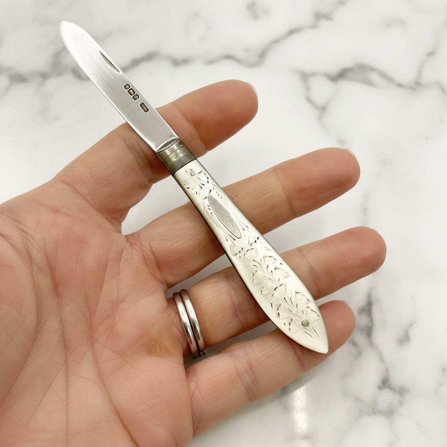 Hand holding a decorative fruit knife with a marble background