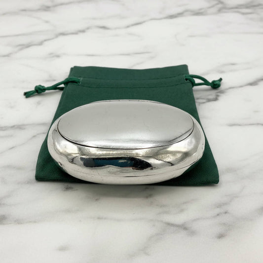 Silver oval box on a green drawstring bag with a marble background