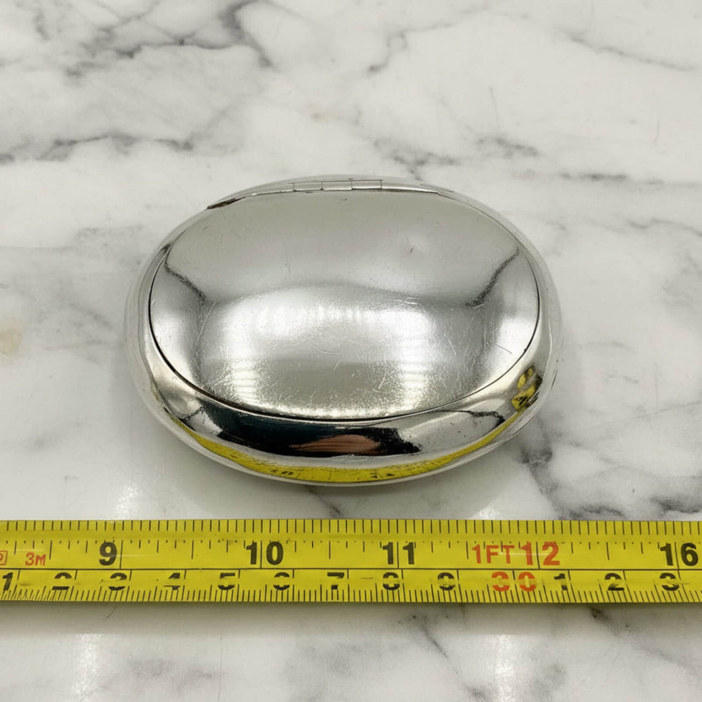 Silver box on a marble surface with a measuring tape for scale.